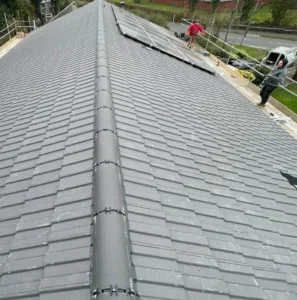 Gray tiled roof with workers installing panels.